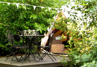 Udendørs plateu med sort smedejernsbord og stole foran et Bedouin Bell Tent, omgivet af grønne planter.