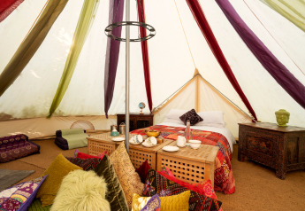 Interior de la tienda Bedouin Bell Tent en Reino Unido con cojines coloridos, cama y muebles tallados.