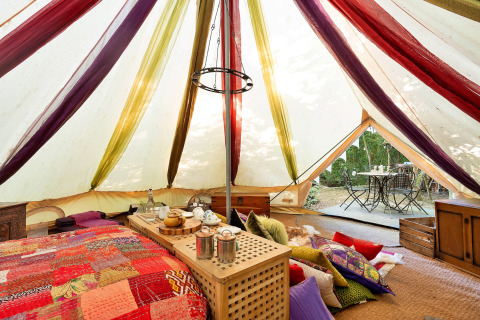 Farverigt indrettet Bedouin Bell Tent i Storbritannien med puder, tæpper og tebord, set indefra.