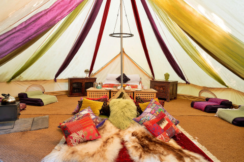 Interiør af Bedouin Bell Tent i Storbritannien, farverige puder, tæpper og lavt træmøblement.