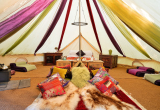 Interiør af Bedouin Bell Tent i Storbritannien, farverige puder, tæpper og lavt træmøblement.