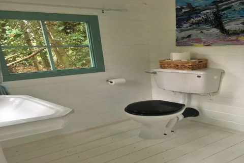 Lyst badeværelse med toilet, håndvask, papirrulleholder og vindue med udsigt til skov, i Bedouin Bell Tent.