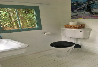 Lyst badeværelse med toilet, håndvask, papirrulleholder og vindue med udsigt til skov, i Bedouin Bell Tent.