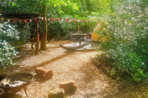 Solbeskinnet lejrplads ved Bedouin Bell Tent i Storbritannien med bålplads, træstubbe og flagguirlande.