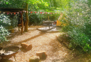 Solbeskinnet lejrplads ved Bedouin Bell Tent i Storbritannien med bålplads, træstubbe og flagguirlande.