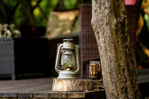 En gammel lanterne og en glaskrukke står på en træstub ved siden af et træ, udendørs ved Bedouin Bell Tent.