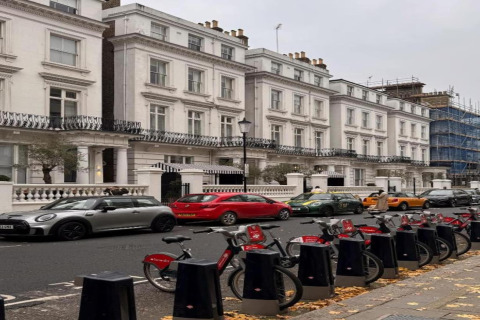 Række hvide byhuse, parkerede biler og lejede cykler på fortovet i et byområde i Storbritannien.