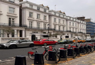 Række hvide byhuse, parkerede biler og lejede cykler på fortovet i et byområde i Storbritannien.