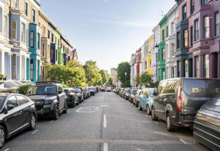 Farverige rækkehuse og parkerede biler langs en gade i Storbritannien på en solrig dag i byen.