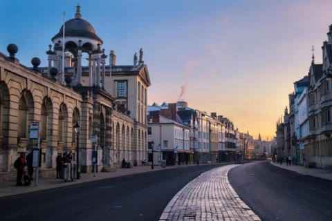 Billede af en historisk gade i Oxford, Storbritannien, ved solnedgang med gamle bygninger og rolig stemning.