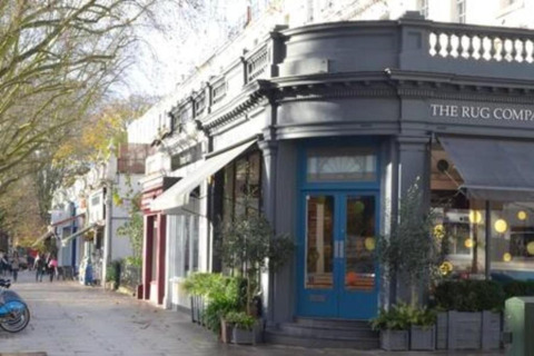 Butiksfacade i London med grå maling, blå dør og udhæng, omkranset af grønne planter.