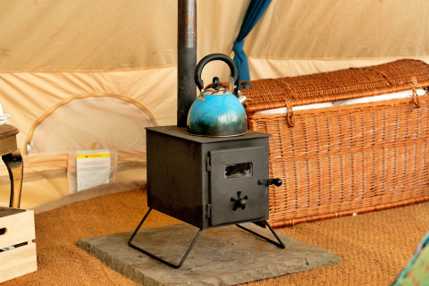 Piccola stufa a legna nera con bollitore blu sopra, all'interno di una tenda teepee marocchina nel Regno Unito.