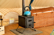 Piccola stufa a legna nera con bollitore blu sopra, all'interno di una tenda teepee marocchina nel Regno Unito.