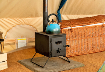 Piccola stufa a legna nera con bollitore blu sopra, all'interno di una tenda teepee marocchina nel Regno Unito.
