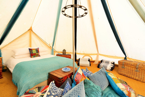 Interni di una tenda Bell marocchina nel Regno Unito con letto accogliente, cuscini e bauli decorativi.