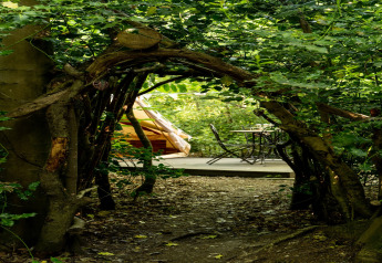 Arco naturale di rami verso la 'Moroccan Bell Tent' con tavolo e sedie nel bosco nel Regno Unito.