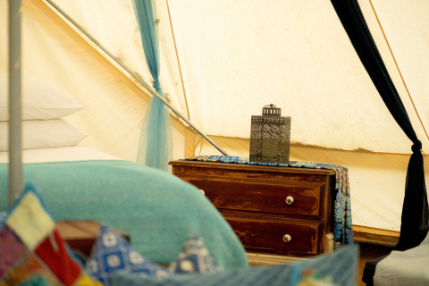 Vista interna del Moroccan Bell Tent nel Regno Unito con cuscini colorati, letto e comodino rustico.