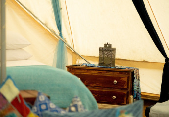 Vista interna del Moroccan Bell Tent nel Regno Unito con cuscini colorati, letto e comodino rustico.