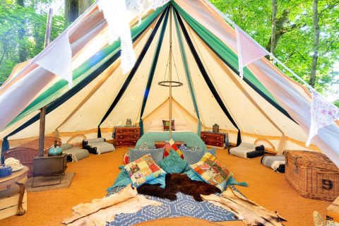 Vista interna della Moroccan Bell Tent nel Regno Unito con cuscini colorati, tappeti e mobili in legno.