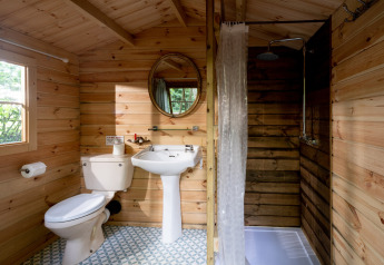 Bagno con pareti in legno, WC, lavabo e doccia in una tenda marocchina nel Regno Unito.