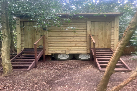 Capanna di legno su ruote con due scale e porte, immersa tra gli alberi vicino alla 'Moroccan Bell Tent' nel Regno Unito.