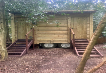 Capanna di legno su ruote con due scale e porte, immersa tra gli alberi vicino alla 'Moroccan Bell Tent' nel Regno Unito.