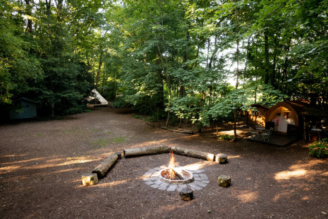 Tenda Moroccan Bell Tent in campeggio con falò, tipi e bosco nel Regno Unito, luce filtrata dagli alberi.