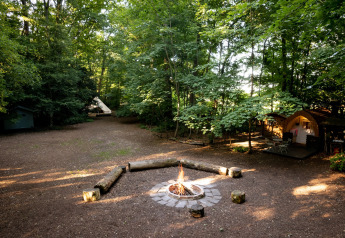 Tenda Moroccan Bell Tent in campeggio con falò, tipi e bosco nel Regno Unito, luce filtrata dagli alberi.