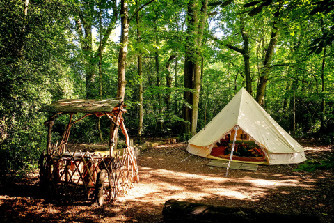 Tenda tipi Moroccan Bell Tent nel bosco nel Regno Unito, con panchina rustica e verde lussureggiante.