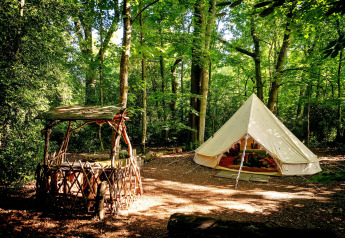 Tenda tipi Moroccan Bell Tent nel bosco nel Regno Unito, con panchina rustica e verde lussureggiante.