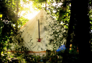La luce del sole filtra tra gli alberi e illumina una tenda tipi 'Moroccan Bell Tent' nel Regno Unito.