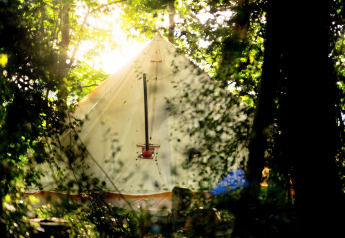 La luce del sole filtra tra gli alberi e illumina una tenda tipi 'Moroccan Bell Tent' nel Regno Unito.