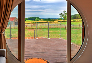 Vista dall'interno di un pod attraverso una porta circolare, su un terrazzo e campi verdi all'esterno.