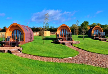 Drie charmante glamping-pods in hout op een groene grasweide onder een heldere hemel, ideaal voor een uitje.