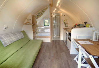 Intérieur d’un pod moderne avec canapé vert, lit double, petite cuisine, coin repas et salle de bain.