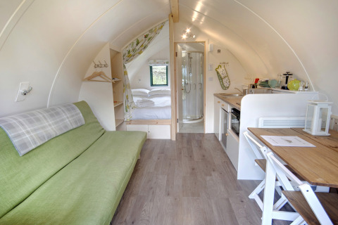 Interieur van een moderne pod met groene bank, tweepersoonsbed, kleine keuken en eigen badkamer.
