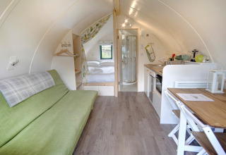 Interieur van een moderne pod met groene bank, tweepersoonsbed, kleine keuken en eigen badkamer.