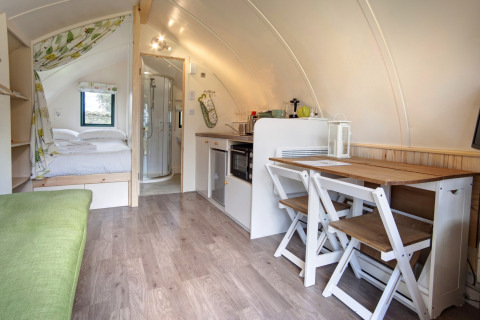 Interieurfoto van een gezellige pod met bed, eettafel, kitchenette en badkamer met douche.