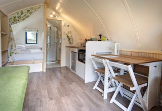 Interieurfoto van een gezellige pod met bed, eettafel, kitchenette en badkamer met douche.