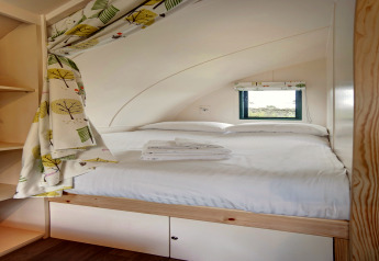 Intérieur cosy d'une cabane avec lit double, petite fenêtre, rideaux à motifs et serviettes pliées.