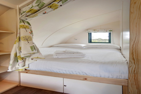 Knus pod-interieur met een tweepersoonsbed, klein raam, vrolijke gordijnen en opgevouwen handdoeken.
