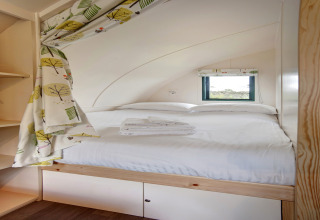 Knus pod-interieur met een tweepersoonsbed, klein raam, vrolijke gordijnen en opgevouwen handdoeken.