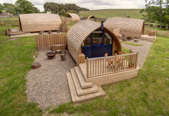 Pods de glamping en bois avec allées en gravier à Blackcleugh Glamping, situés dans la campagne britannique.