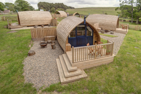 Houten glampingpods met grindpaden en terrassen bij Blackcleugh Glamping in het Britse platteland.