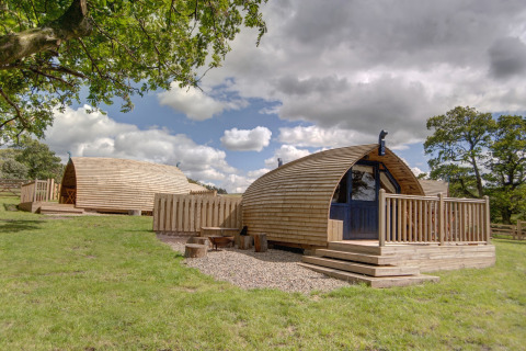 Houten glamping-pods bij Blackcleugh Glamping op grasveld onder een blauwe lucht met wolken.