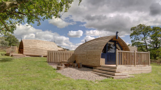 Træ glamping-pods på Blackcleugh Glamping under en blå himmel med skyer og grønt græs omkring.