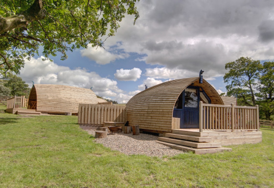 Houten glamping-pods bij Blackcleugh Glamping op grasveld onder een blauwe lucht met wolken.