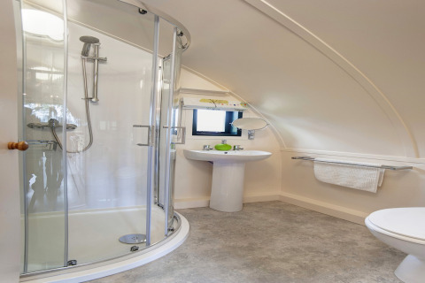 Moderne badkamer in een pod met gebogen douchecabine, wastafel, handdoekrek en schuin plafond.