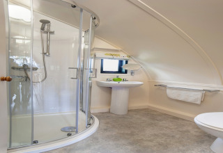 Moderne badkamer in een pod met gebogen douchecabine, wastafel, handdoekrek en schuin plafond.