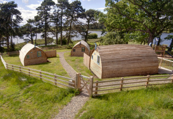 Pods en bois à Blackcleugh Glamping au Royaume-Uni, entourés de pelouse et clôtures près d’un lac.